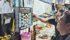 PANTAUJADWAL PIALA DUNIA – Arief dan Memet memperhatikan jadwal pertandingan Piala Dunia 2026 pada poster kecil sambil menikmati mi di Warung Kai Adi, Banjarmasin. Demam Piala Dunia mulai terasa di kalangan pencinta sepak bola yang bersiap begadang mendukung tim favorit mereka. (foto: Mercy )