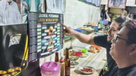PANTAUJADWAL PIALA DUNIA – Arief dan Memet memperhatikan jadwal pertandingan Piala Dunia 2026 pada poster kecil sambil menikmati mi di Warung Kai Adi, Banjarmasin. Demam Piala Dunia mulai terasa di kalangan pencinta sepak bola yang bersiap begadang mendukung tim favorit mereka. (foto: Mercy )